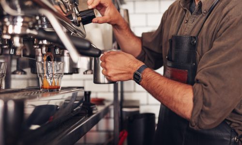 Cropped shot of barista using a coffee maker to prepare a cup of coffee. Cafe worker making a coffee.